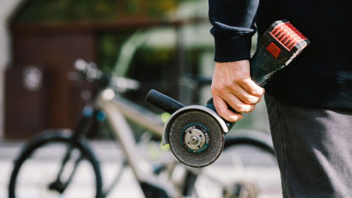 Dieb hält eine Akku-Flex in der linken Hand, im Hintergrund steht ein E-Bike.